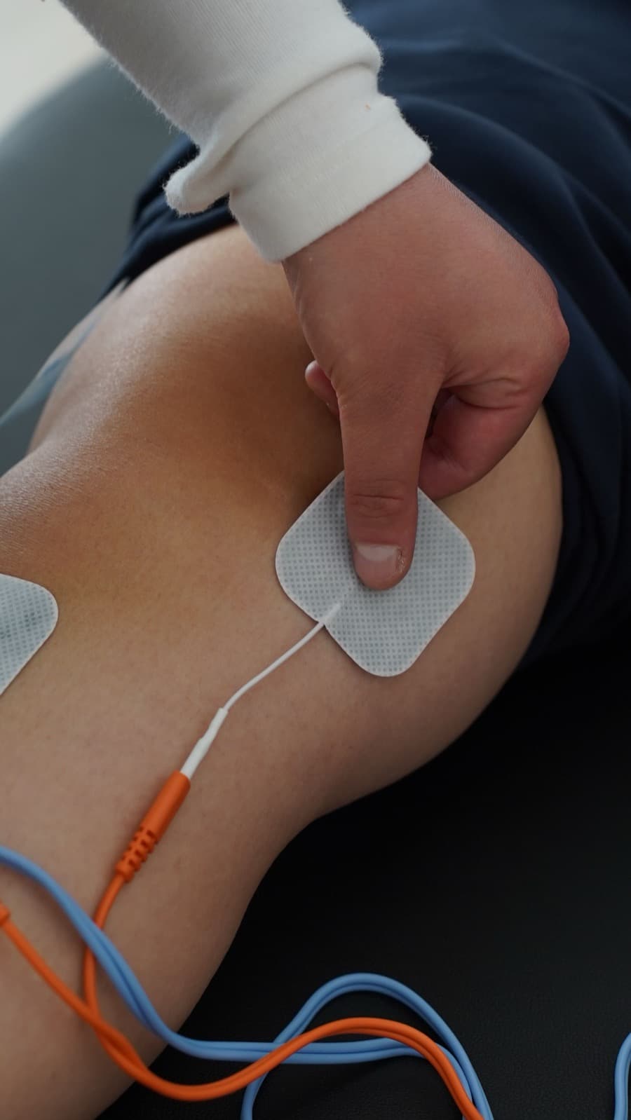 Profesional aplicando electroestimulación con electrodos sobre la rodilla de un paciente
